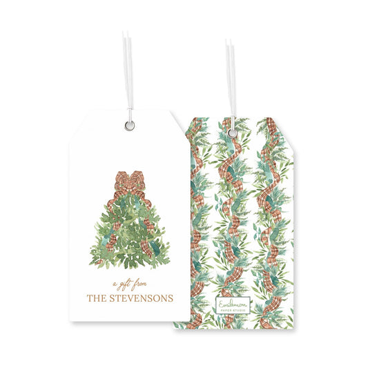 two white tags with Christmas-themed designs hanging from strings. The tag on the left has a Christmas tree design with pine cones, and the tag on the right has a repeating pattern of green leaves and pine branches.