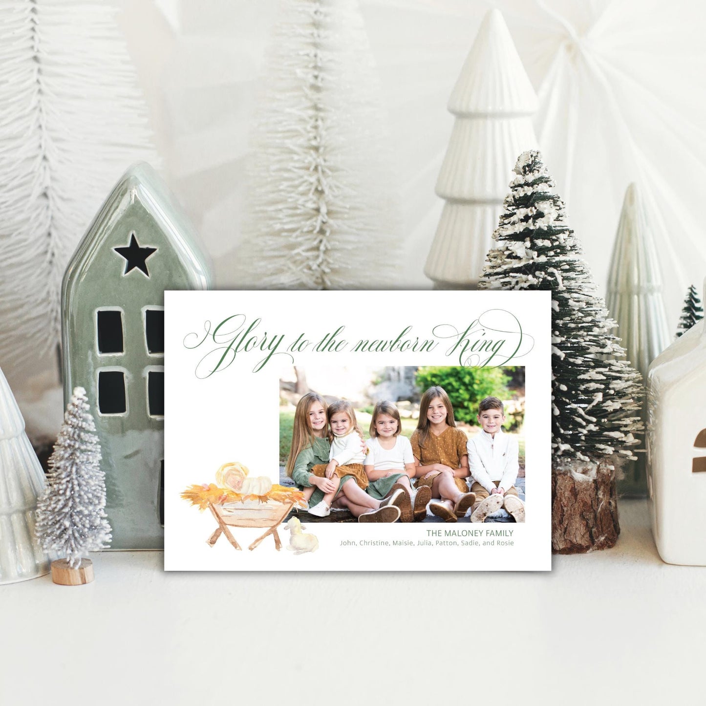 A white card with a photo of a family sitting in a nativity scene, surrounded by Christmas decorations and trees.
