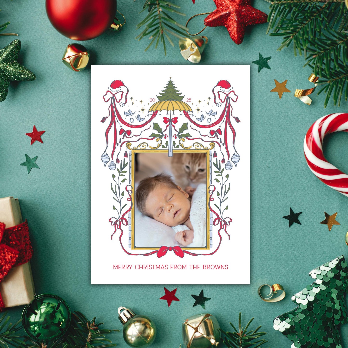 A Christmas card with a photo of a sleeping baby surrounded by various holiday decorations, including ornaments, tinsel, and a star.