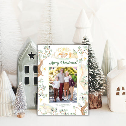 A family photo is displayed in front of a Christmas card with a festive design, surrounded by small white ceramic ornaments and a miniature tree.