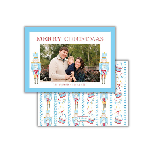 A family photo is displayed in a blue frame, with the text &quot;MERRY CHRISTMAS&quot; written above it. The frame also features nutcracker characters and a pattern of nutcrackers and other Christmas-themed elements.