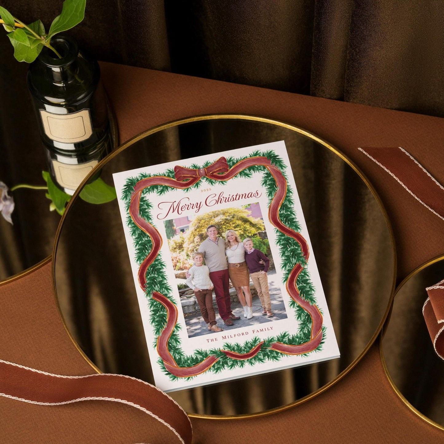 A round glass plate with a framed photo of a family, surrounded by a wreath, sits on a brown table.