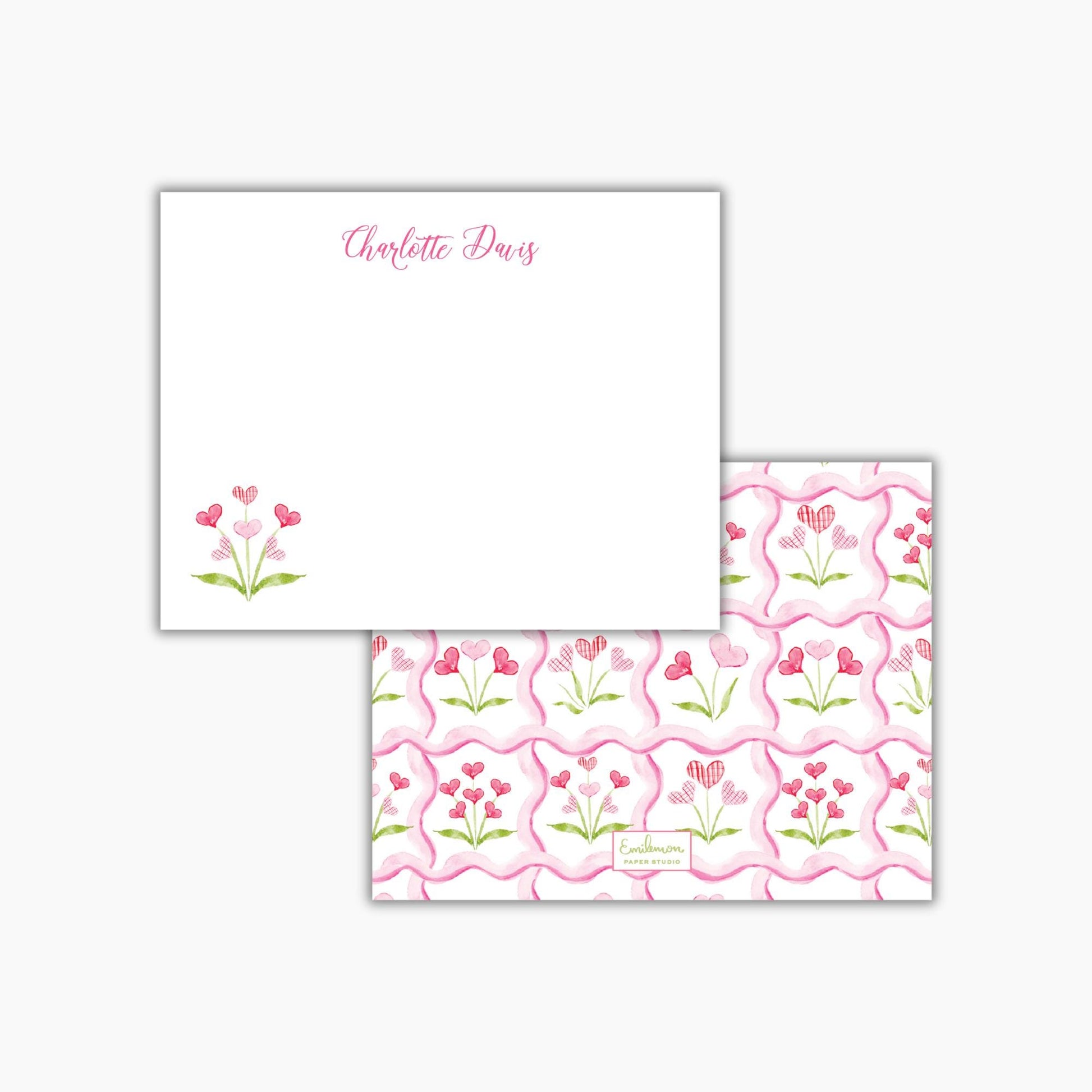 a white square note card with a floral design and the name "Charlotte Davis" written on it. The card also features a repeating pattern of pink hearts and flowers on the right side.