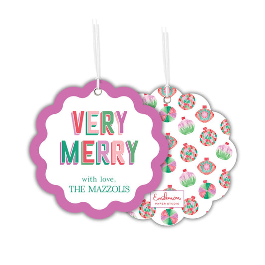 two circular tags hanging from strings. The tag on the left has a scalloped edge and a pink background, with the text &quot;VERY MERRY with love, THE MAZZOLIS&quot; written in a colorful font. The tag on the right has a white background with a pattern of colorful Christmas ornaments.