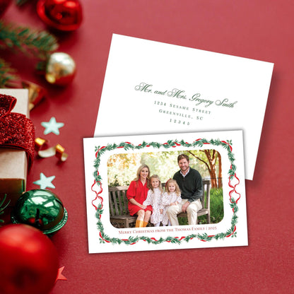 A Christmas card with a family photo of a man, woman, and two children sitting on a bench, surrounded by holiday decorations such as ornaments, tinsel, and a star.