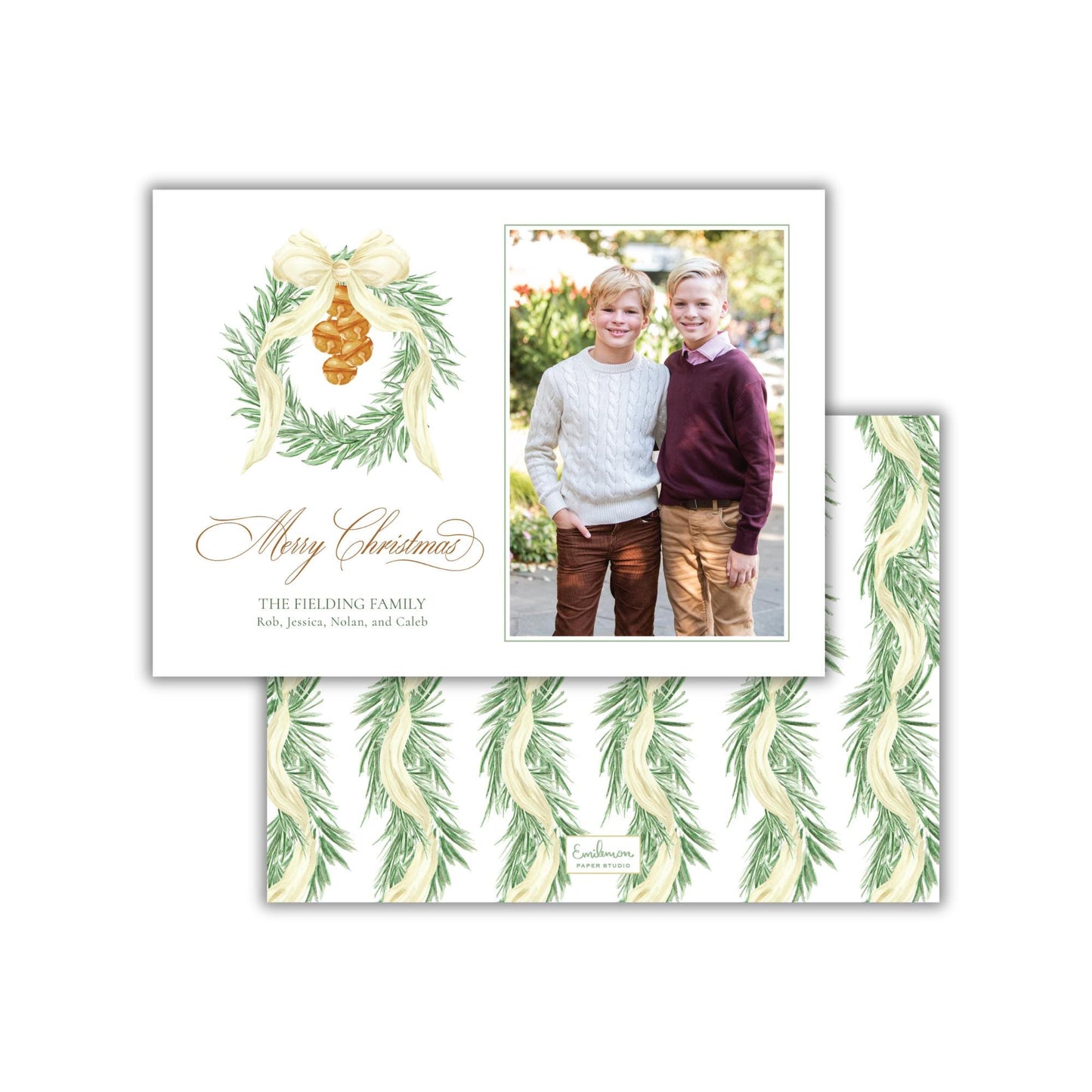 A Christmas card featuring two young boys posing together in front of a wreath. The card has a festive design with a bow and greenery, and includes a photograph of the two boys.