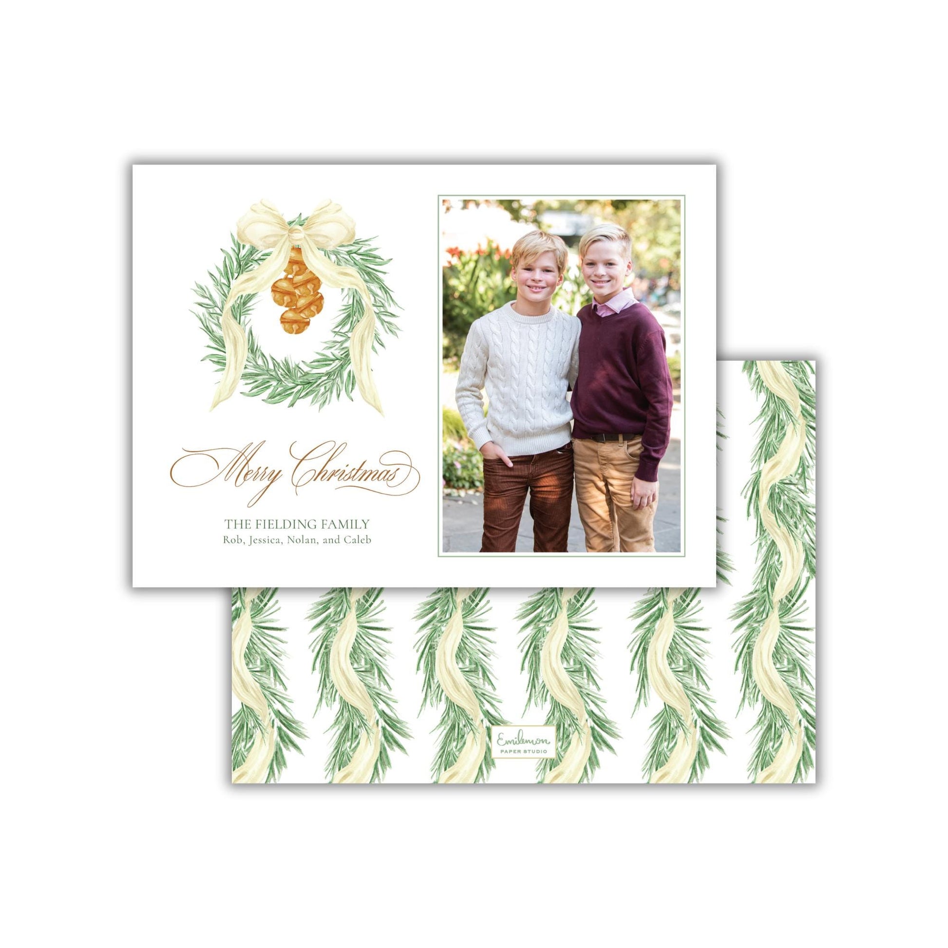 A Christmas card featuring two young boys posing together in front of a wreath. The card has a festive design with a bow and greenery, and includes a photograph of the two boys.