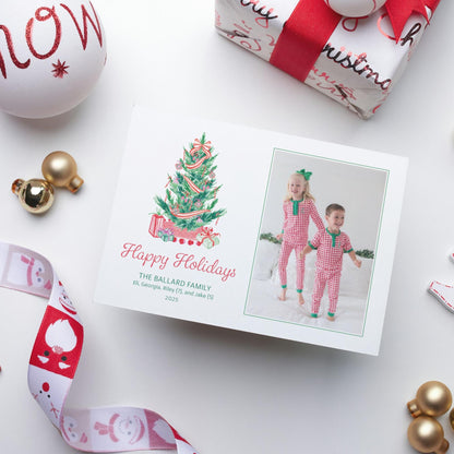 A holiday card featuring two children in red and white checkered pajamas, with a Christmas tree and presents, surrounded by ornaments and a gift box.