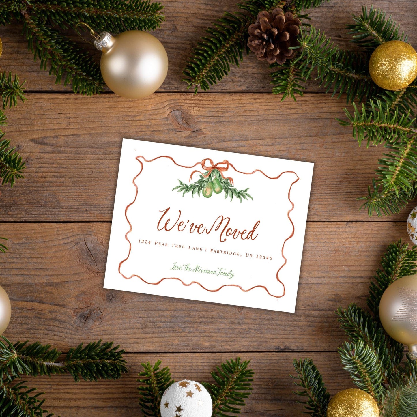 A white card with a festive design, surrounded by Christmas ornaments and greenery, sits on a wooden surface.