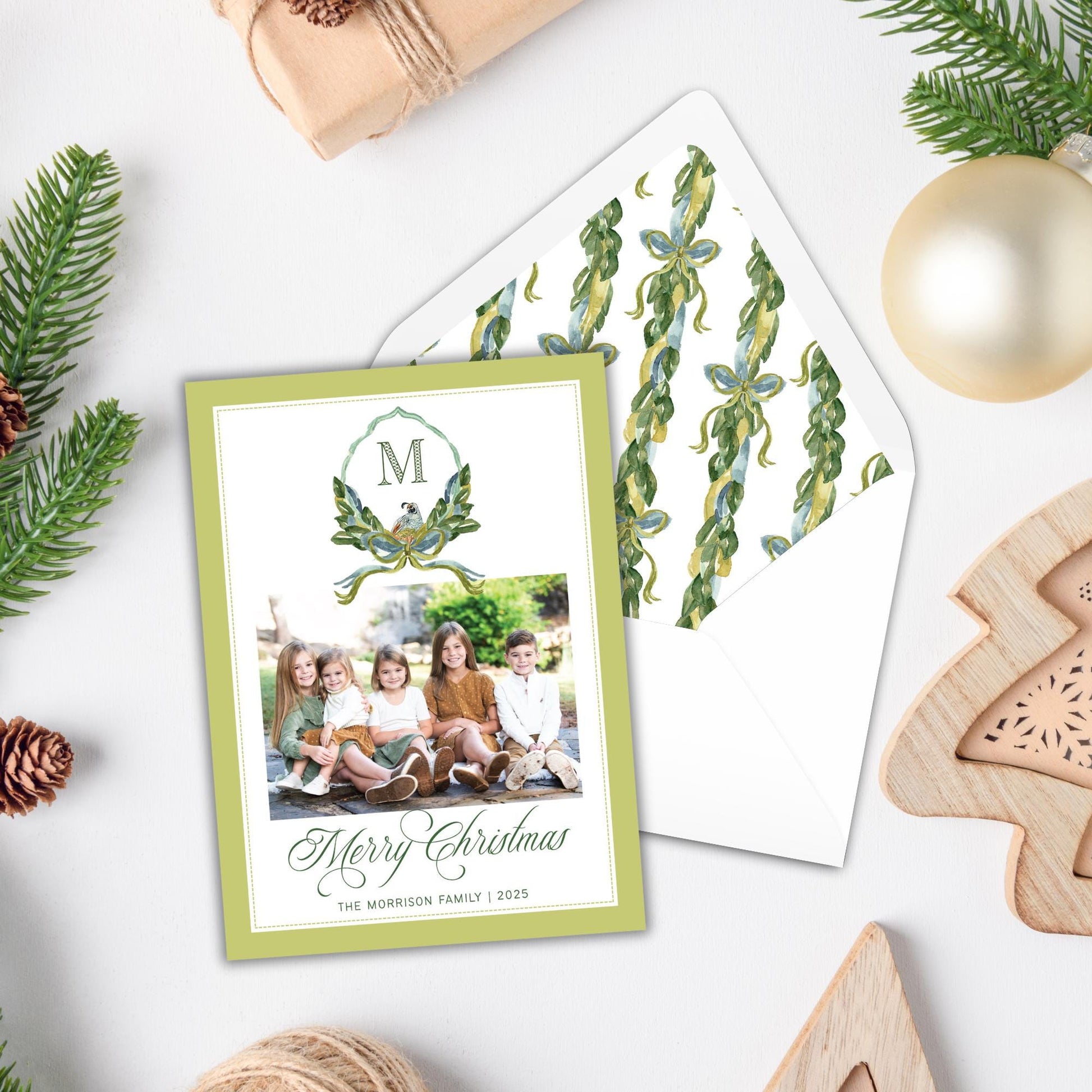 A green Christmas card with a photo of a family sitting together, surrounded by holiday decorations such as pine cones, a Christmas tree, and ornaments.