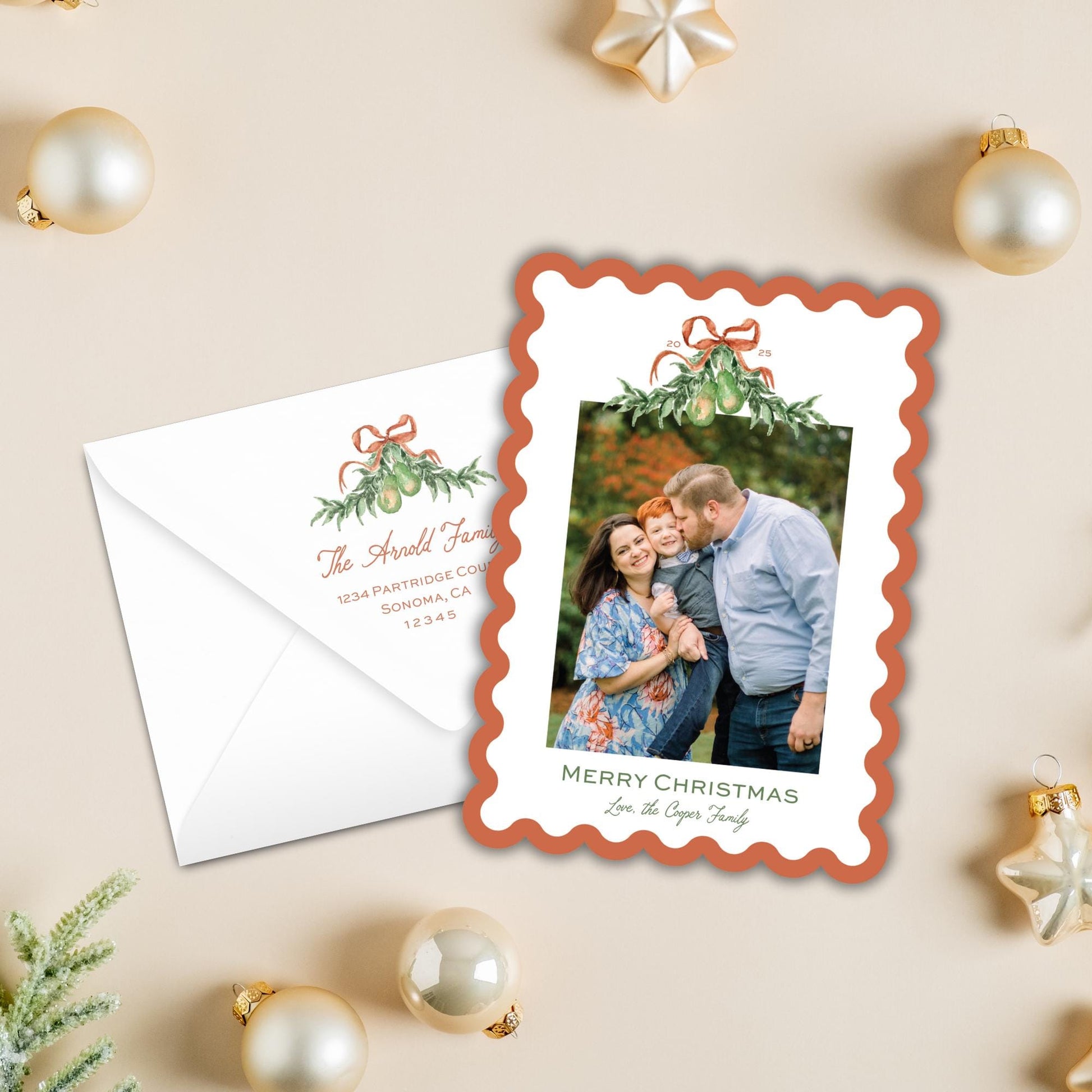 a Christmas card with a photo of a family, along with an envelope and ornaments on a table.