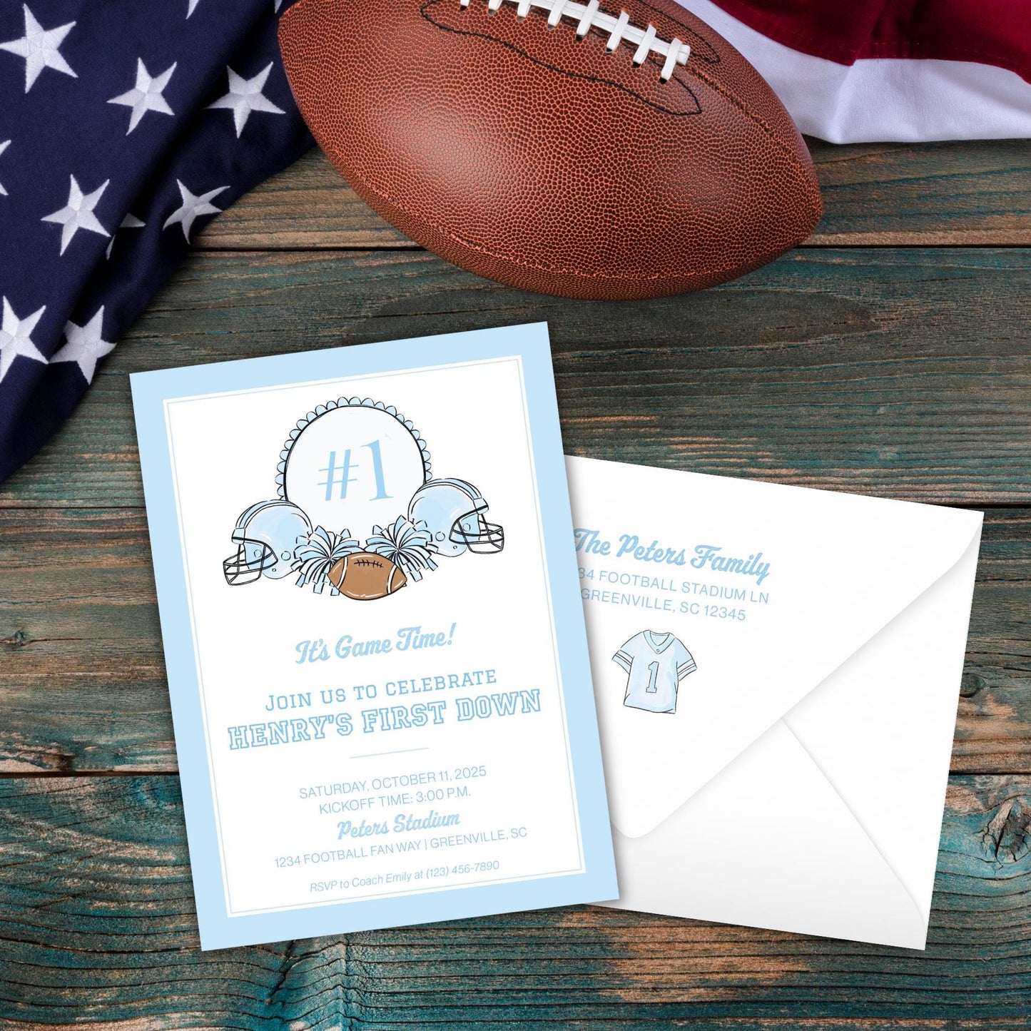 a blue invitation card with a football and an American flag, along with an envelope, all placed on a wooden surface.