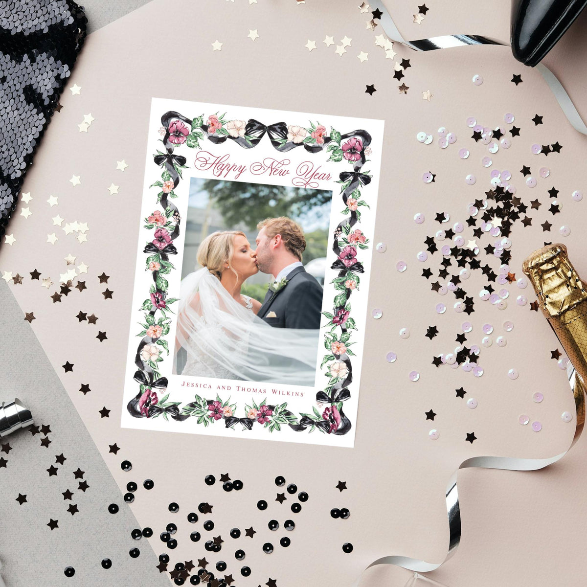 A wedding invitation card with a couple kissing in the center, surrounded by confetti, sequins, and a champagne bottle.