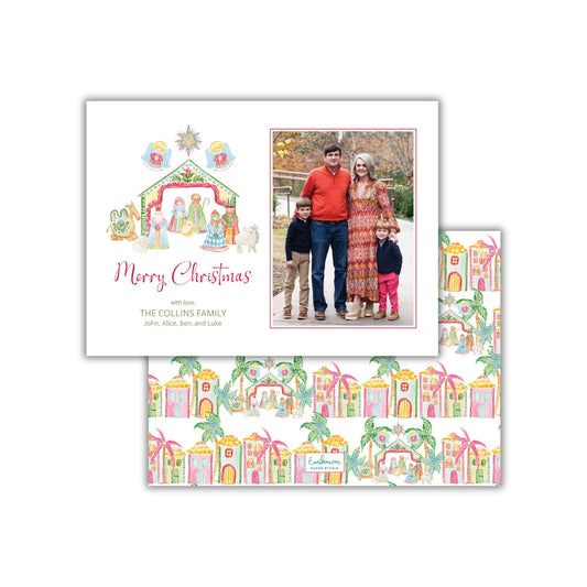 A Christmas card featuring a family photo and a nativity scene with a star above it. The card has a repeating pattern of colorful houses and palm trees on the lower part.