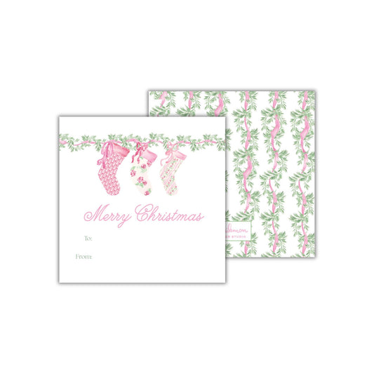 The image is a gift card design with a Christmas theme. It features a pattern of pink and green stockings hanging from a garland, along with the text &quot;Merry Christmas&quot; and &quot;To: From:&quot; printed on it.