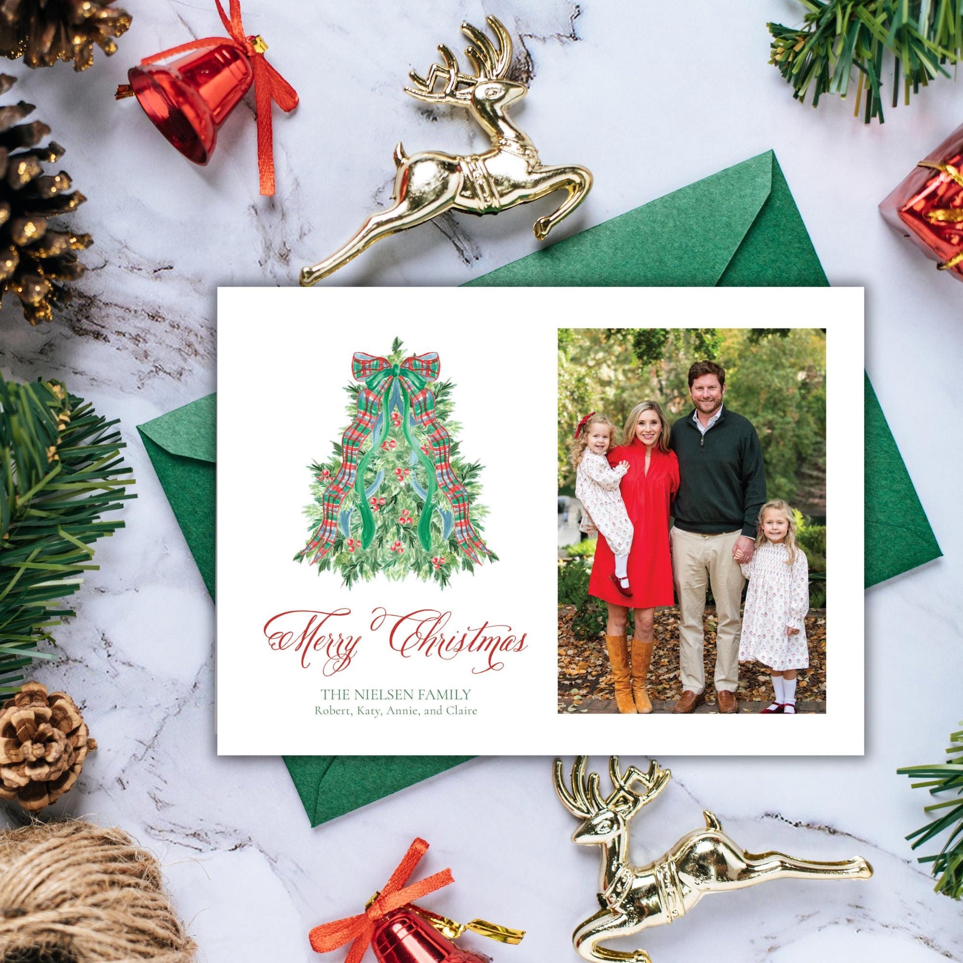 A Christmas card featuring a family photo and a Christmas tree illustration, surrounded by holiday decorations such as pine cones, ornaments, and a bell.