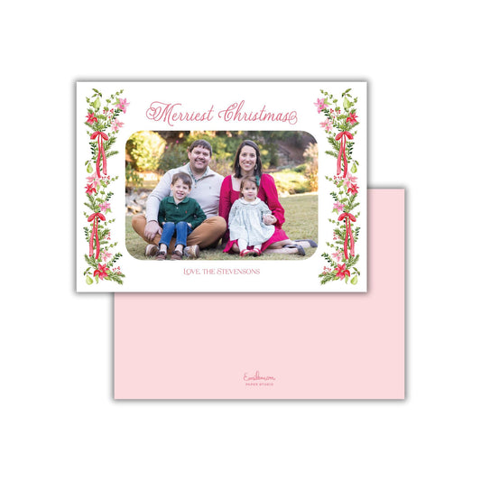 A family portrait of a man, woman, and two children sitting together on a grassy area, with a floral border around the photo.