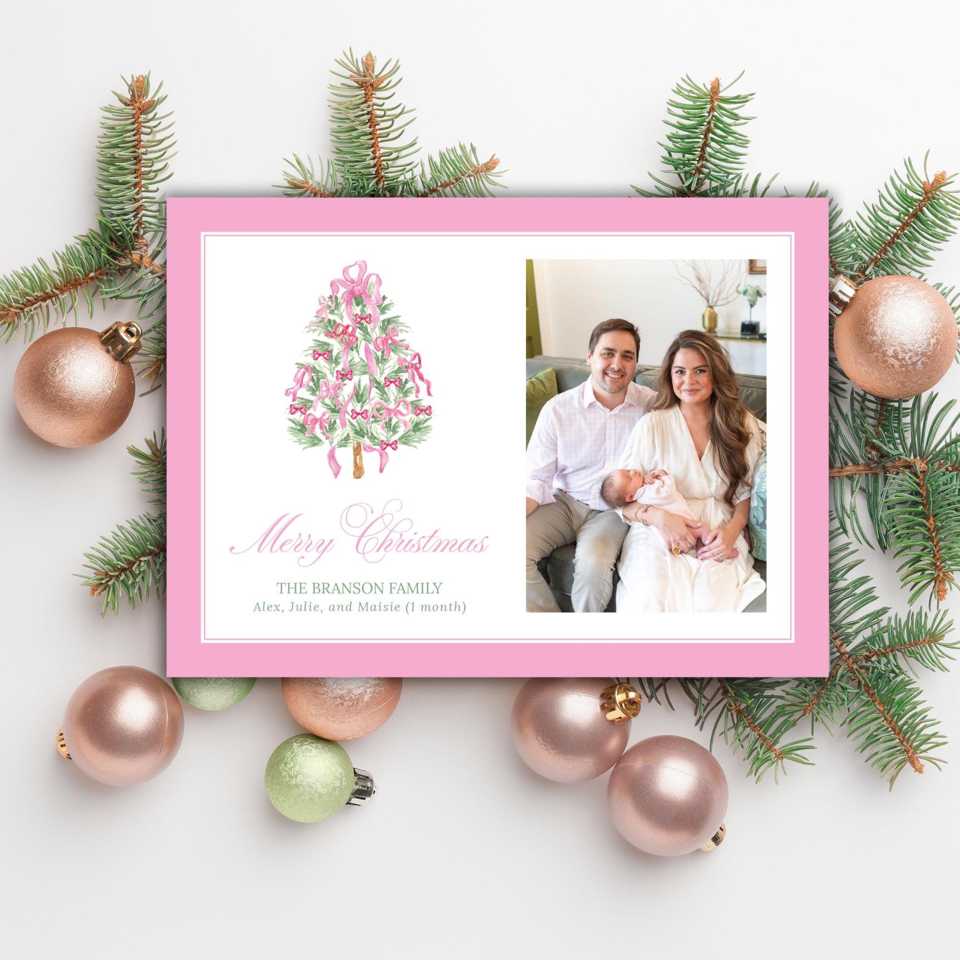 A pink Christmas card with a photo of a family, surrounded by Christmas ornaments and pine branches.