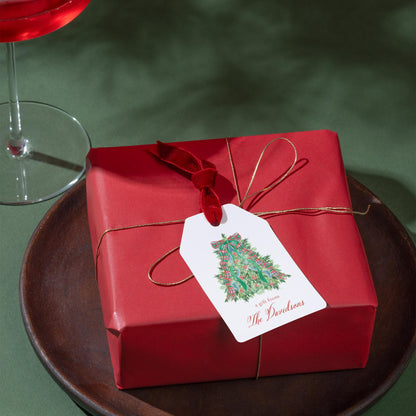 A red gift box with a white tag that reads "a gift from The Davidsons" is placed on a wooden plate, accompanied by a glass of red wine.