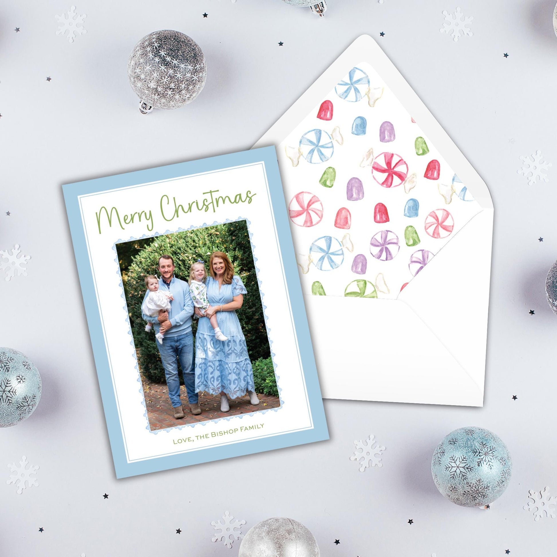 A Christmas card with a family photo and a matching envelope, surrounded by ornaments and snowflakes on a white background.