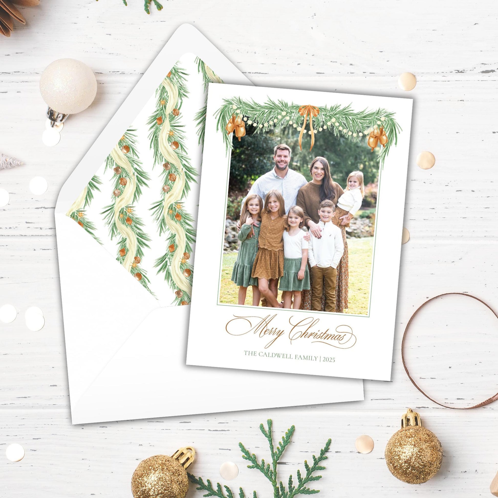 A family photo is displayed on a white card, surrounded by Christmas decorations such as ornaments, pine cones, and greenery.