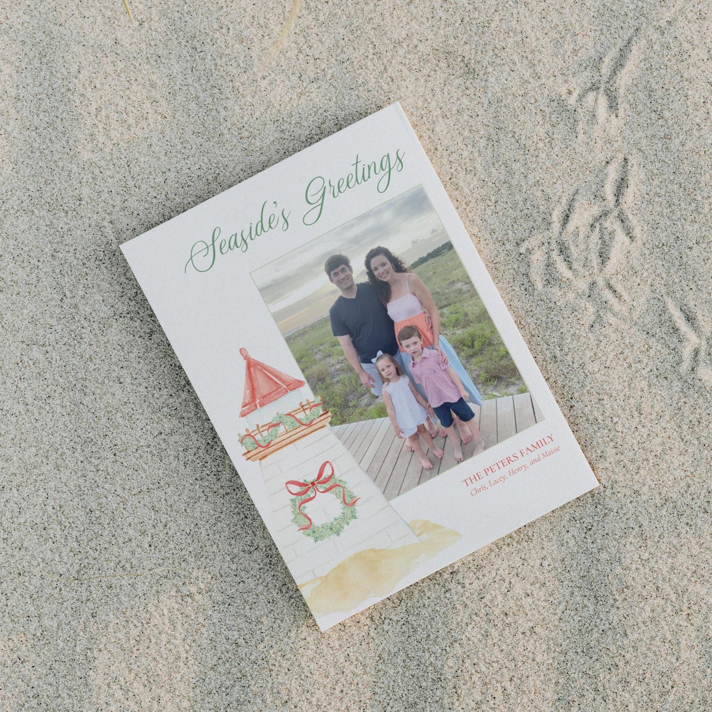 A family photo is displayed on a white card with a red bow, placed on a sandy beach.