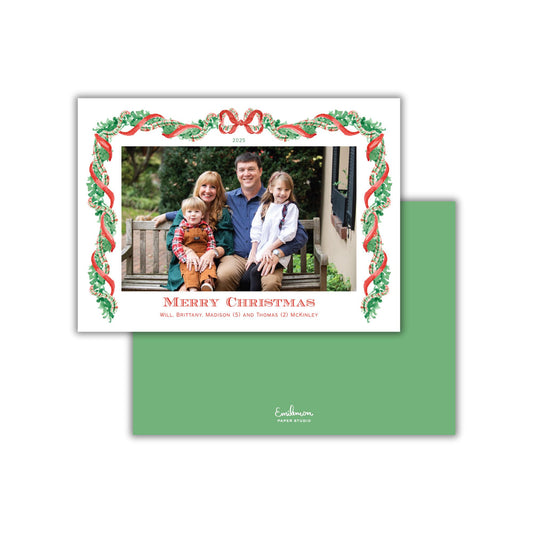 A family photo of a man, woman, and two children sitting on a bench, framed by a decorative border with a Christmas tree design.