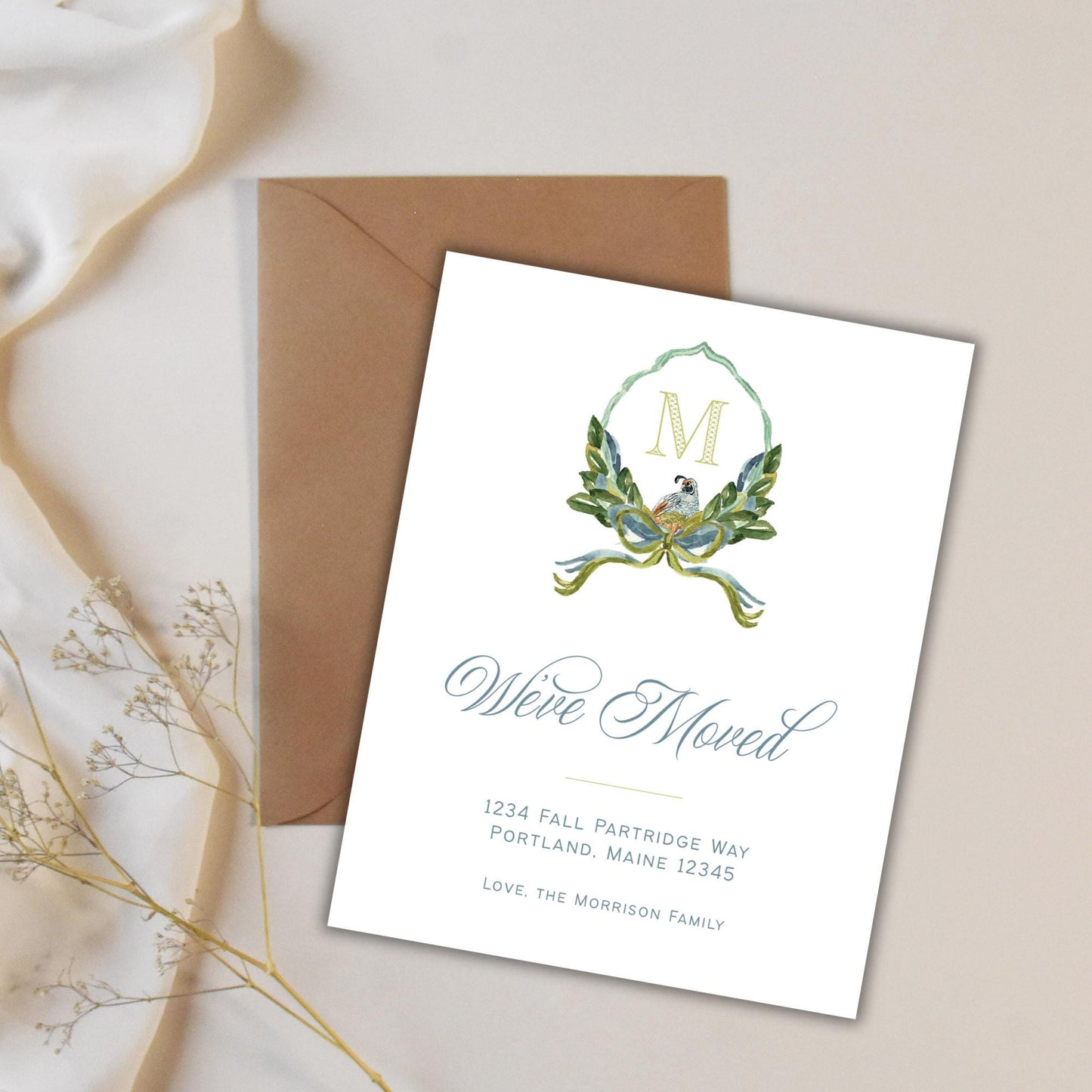 a white card with a brown envelope on a white background. The card has a decorative design and text that reads &quot;We&#39;re Moving&quot; and includes the address &quot;1234 Fall Partridge Way Portland Maine 12343&quot;.