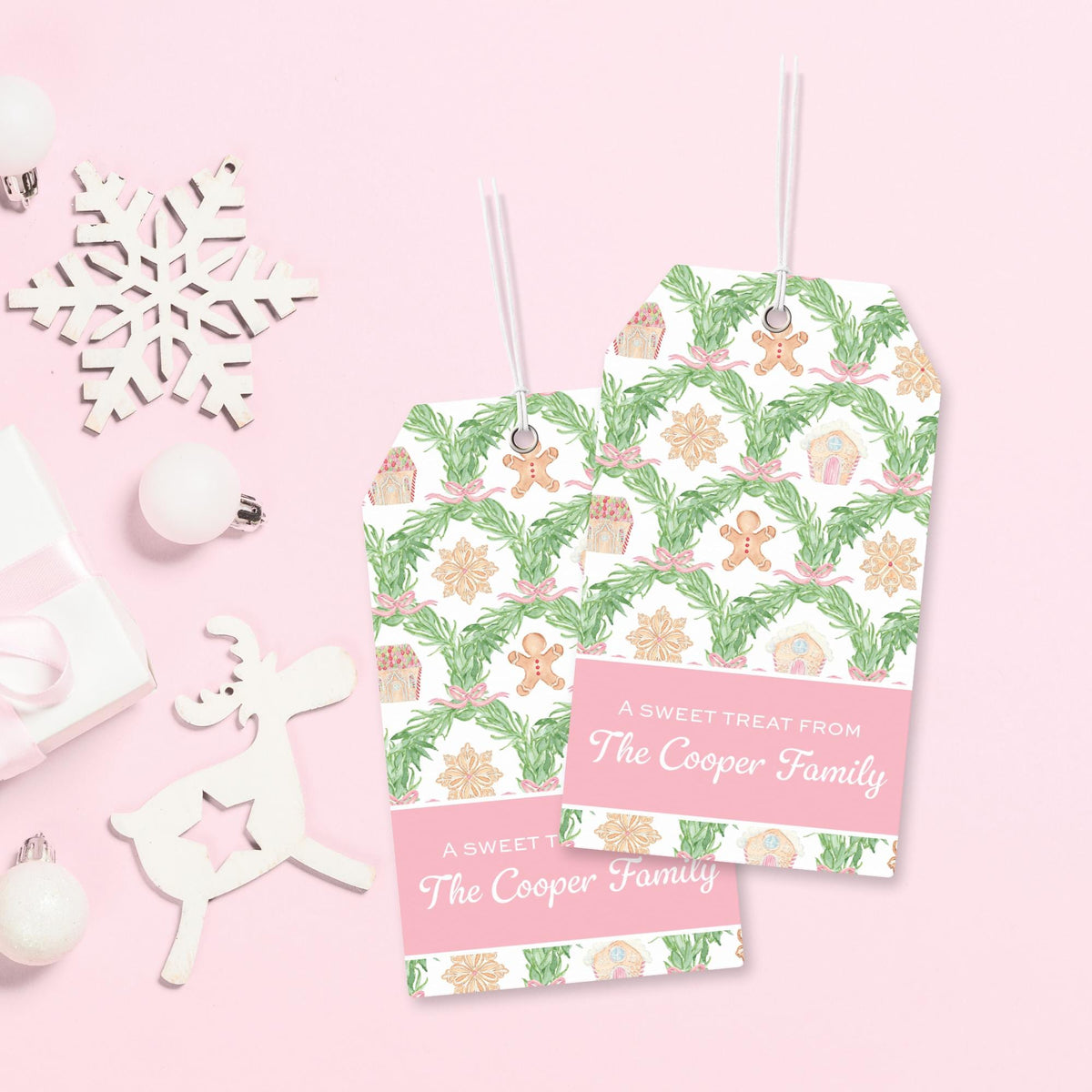 two tags with a festive holiday pattern, hanging on a pink background. There are also some ornaments and a snowflake decoration in the background.