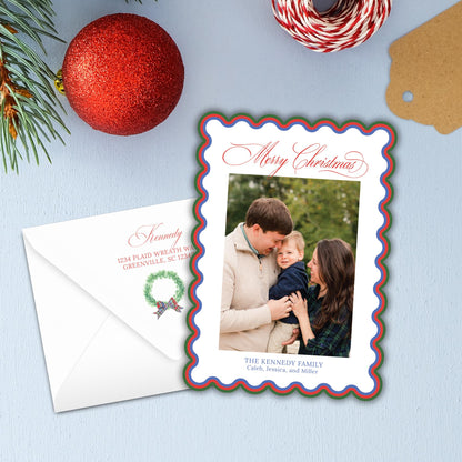 A Christmas card with a family photo of a man, woman, and child, along with a wreath and a red ornament, all placed on a blue background.