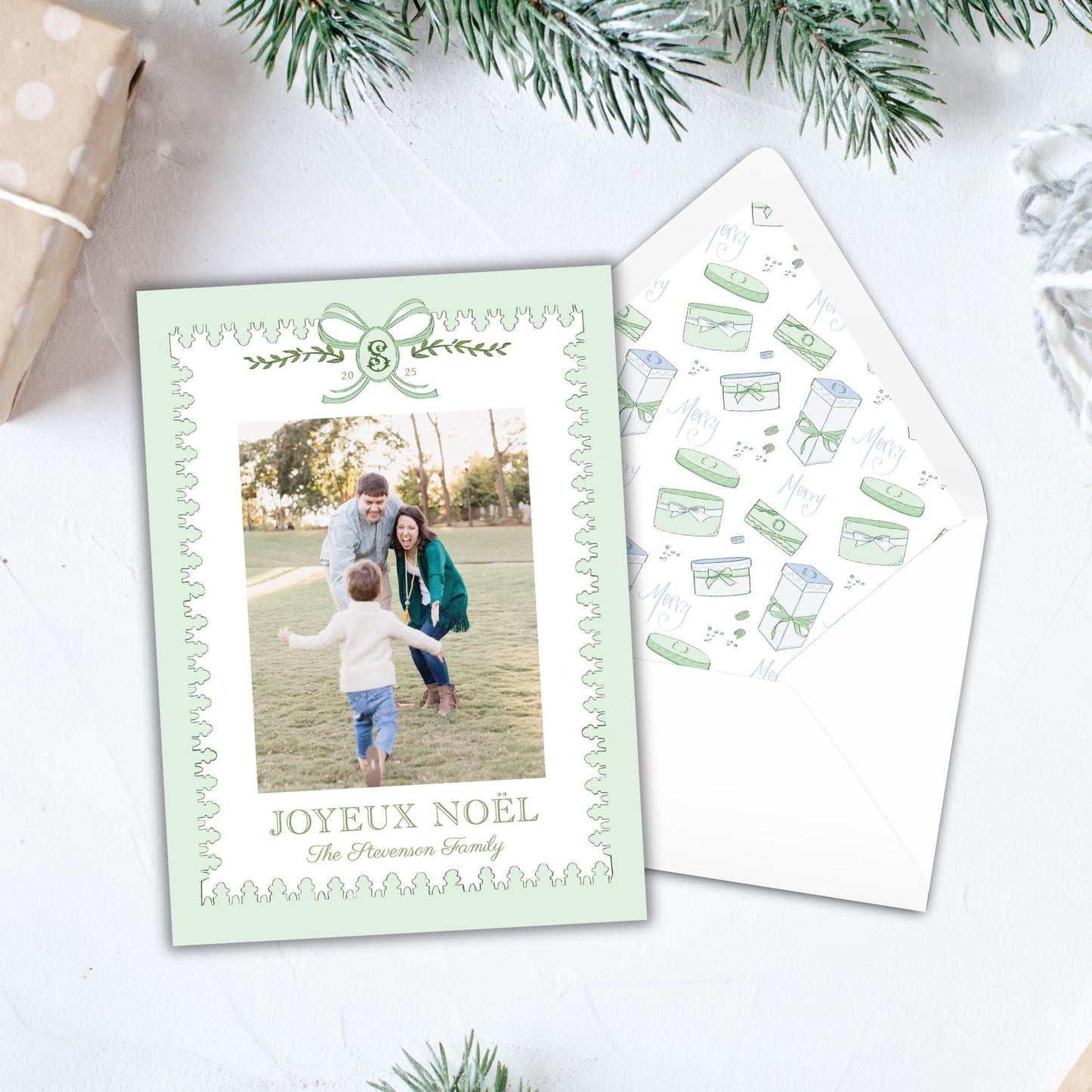 A green holiday card with a photo of a family, and an envelope with a pattern of Christmas presents.