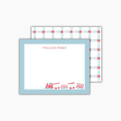 A rectangular notecard with a light blue border and a hand-painted watercolor train in red and blue is in the bottom right corner. The child's name is at the top in a classic red font. The back features a light blue and red geometric pattern.
