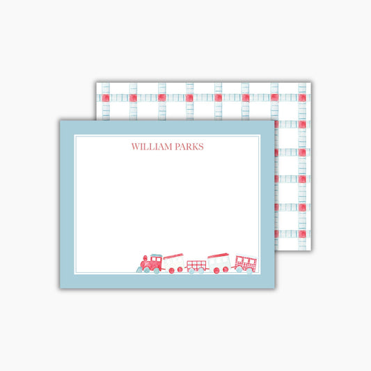 A rectangular notecard with a light blue border and a hand-painted watercolor train in red and blue is in the bottom right corner. The child's name is at the top in a classic red font. The back features a light blue and red geometric pattern.