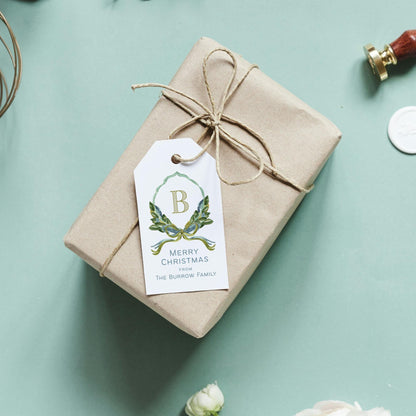 A beige gift box wrapped in brown paper with a white tag featuring a green and gold design and the letter "B" on it, placed on a light blue background.