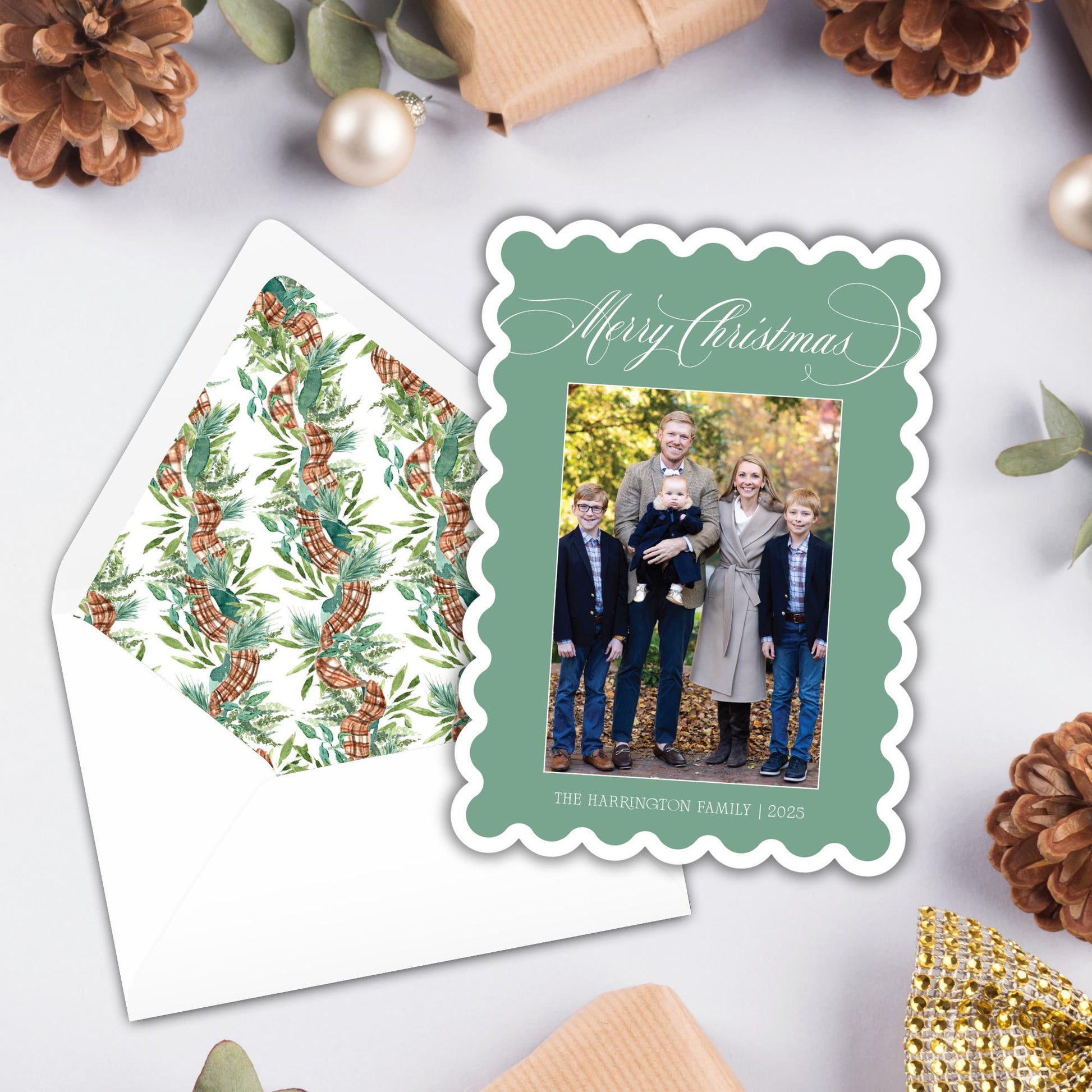 A Christmas card with a family photo of a man, woman, and two children, along with a scalloped edge and a floral pattern, placed on top of a white envelope.