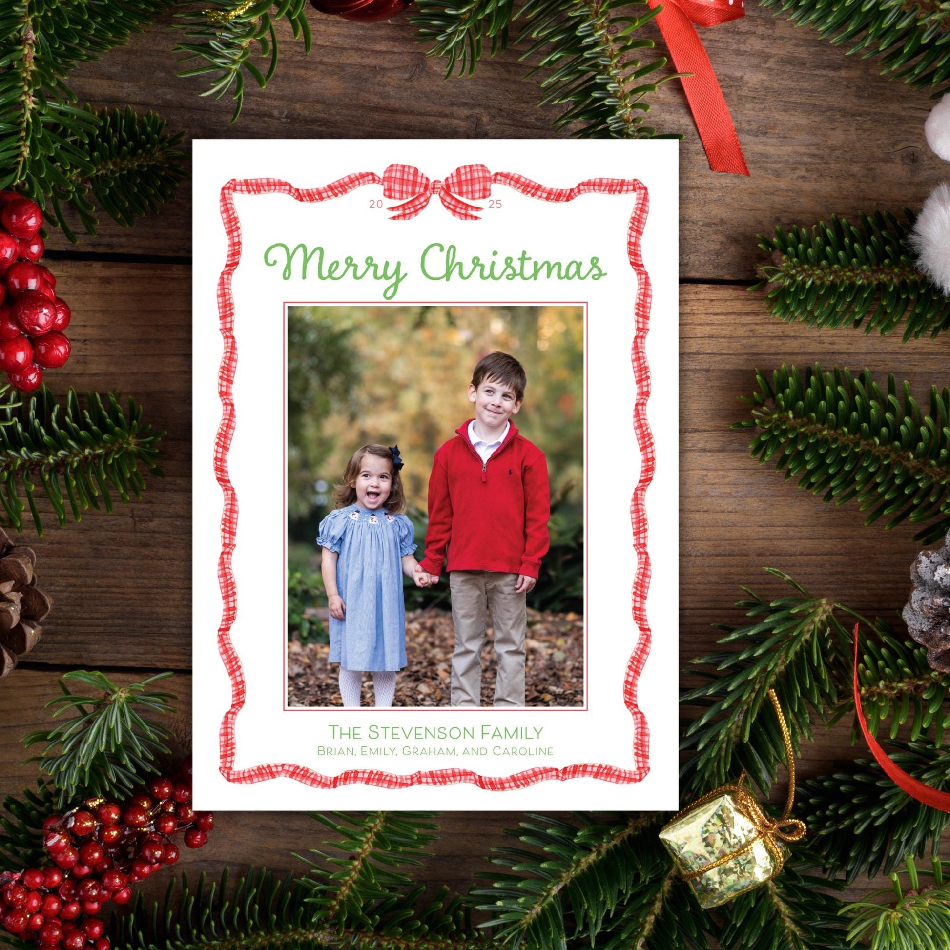 A Christmas card with a photo of two children, a boy and a girl, surrounded by holiday decorations such as pine branches, berries, and a red ribbon.