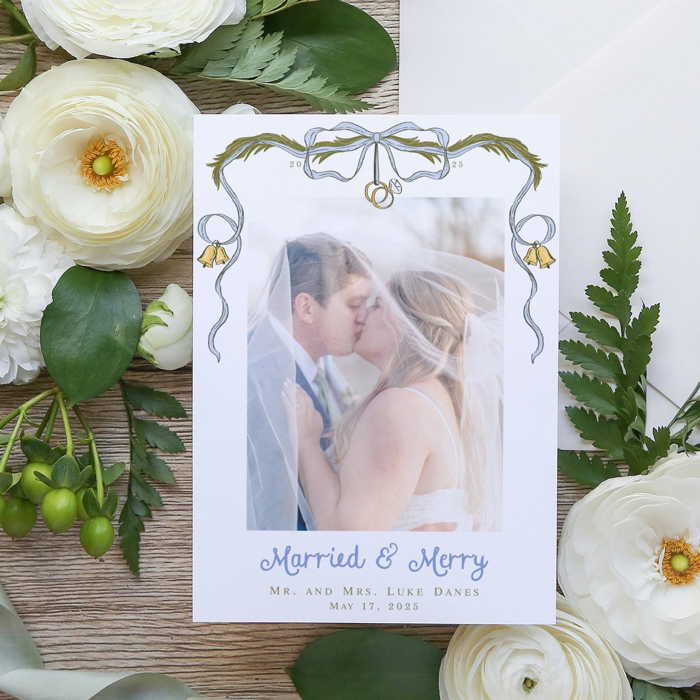 A wedding invitation card with a photo of a couple kissing, surrounded by white flowers and greenery.