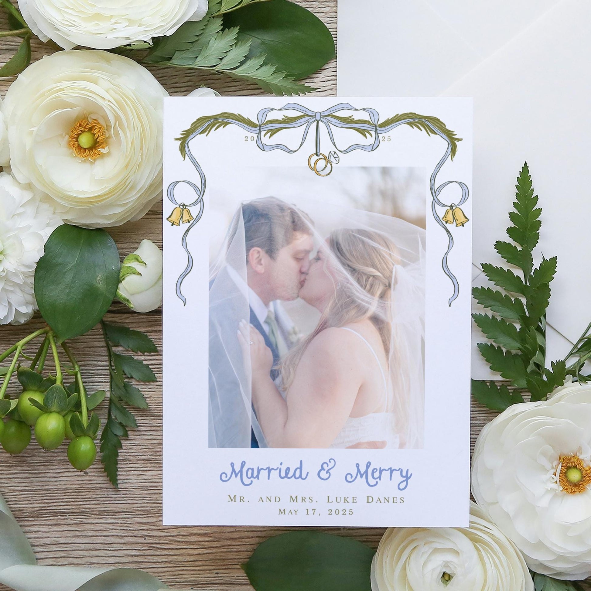 A wedding invitation card with a photo of a couple kissing, surrounded by white flowers and greenery.