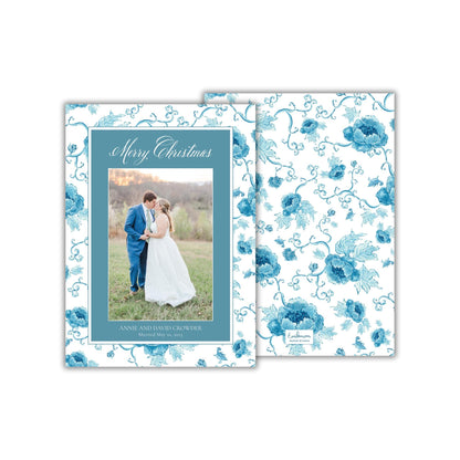 A wedding invitation card with a couple standing in a field, surrounded by a floral pattern in shades of blue.