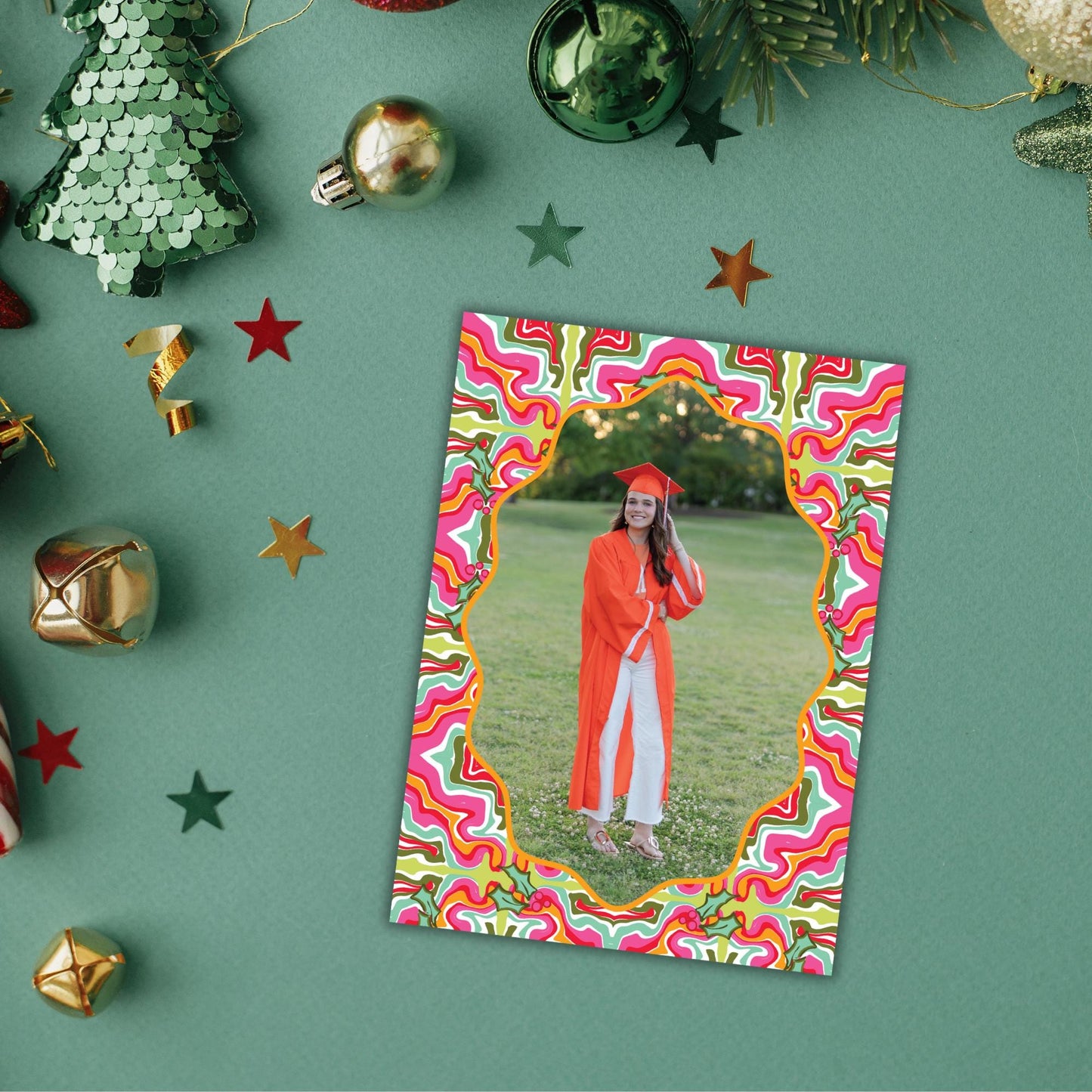 A framed photo of a smiling woman in a graduation gown is displayed on a green background, surrounded by Christmas ornaments and star decorations.