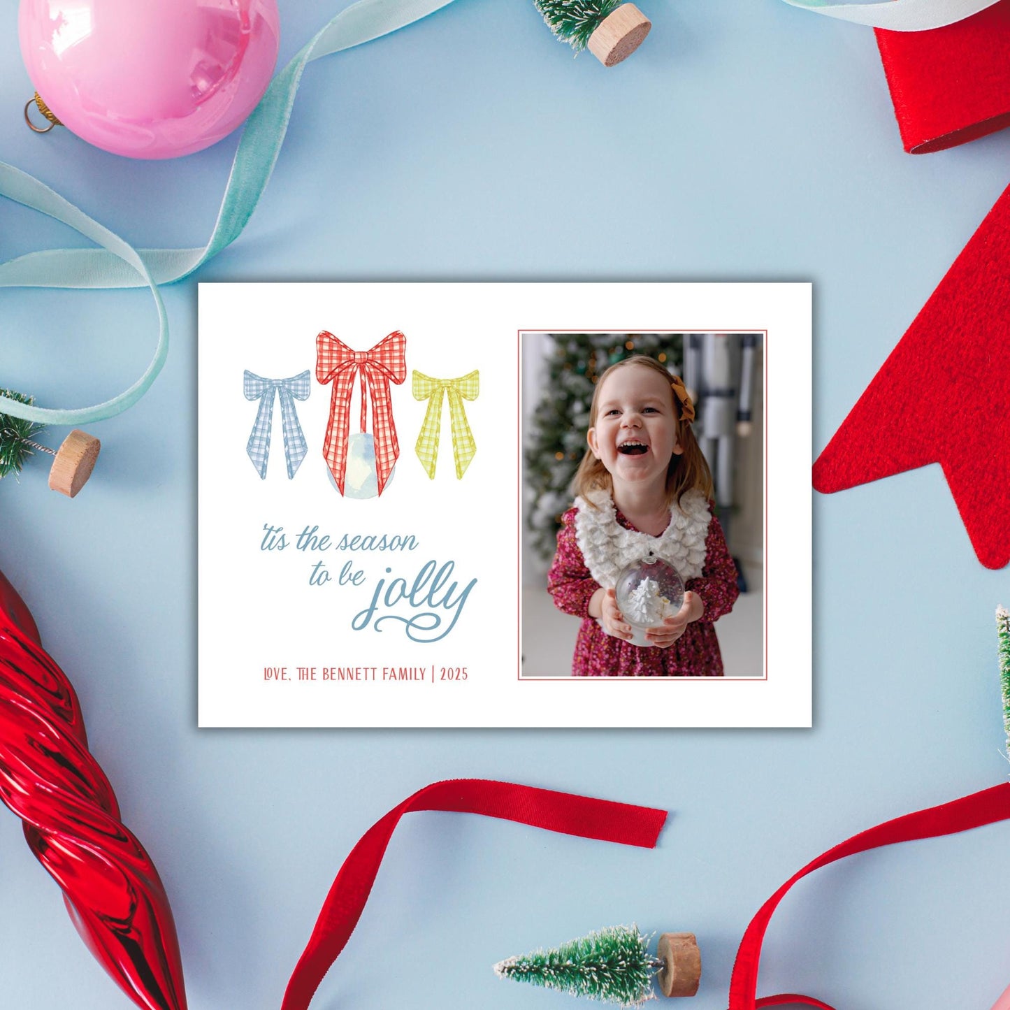 A white card with a photo of a young girl smiling, surrounded by Christmas decorations such as ribbons, ornaments, and a small Christmas tree.