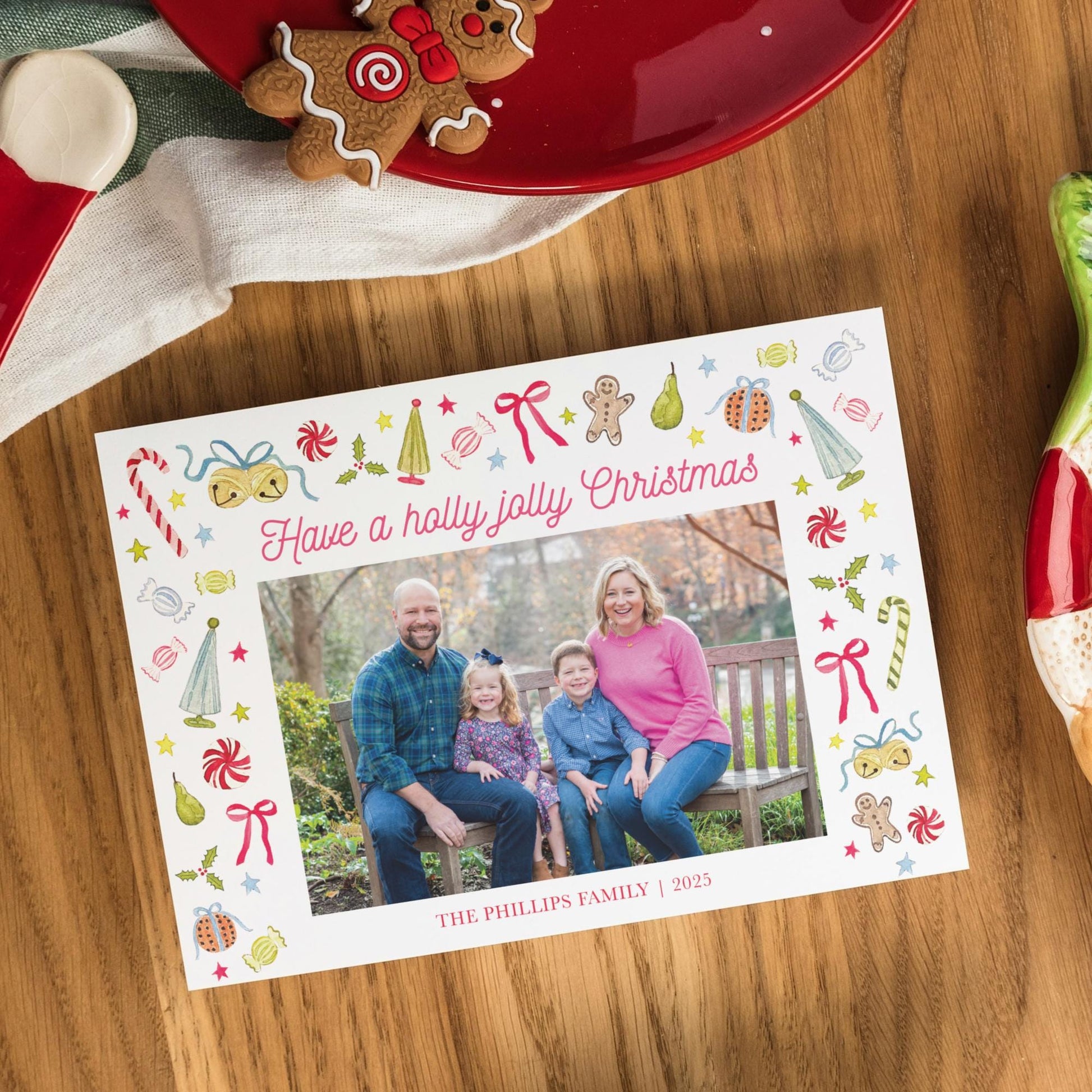 A family photo is displayed on a white card with a festive border, surrounded by holiday decorations such as gingerbread cookies and a red plate.