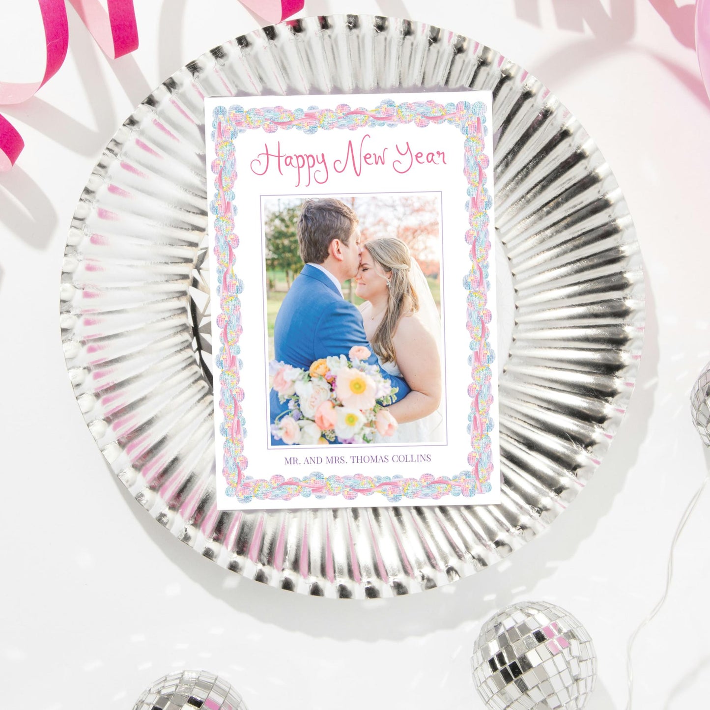 A wedding invitation card with a photo of a couple embracing, surrounded by decorative elements such as ribbons and disco balls.
