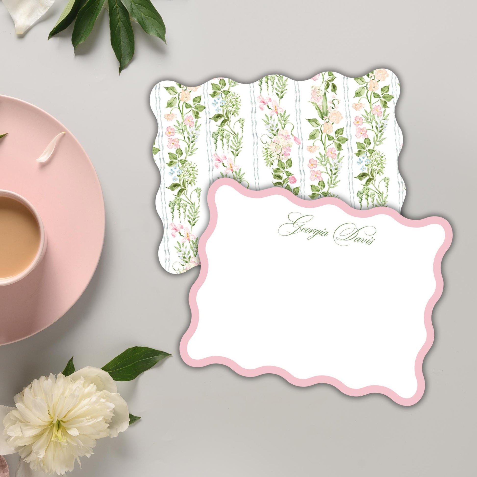 a pink teacup, a white card with a floral pattern, and some white flowers on a gray background.