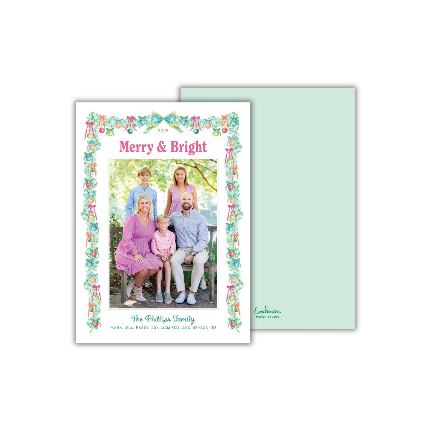 A family portrait of a group of people, including adults and children, sitting together in a garden setting. The text on the card reads &quot;Merry & Bright&quot; and &quot;The Phillips Family&quot; along with additional text that is too small to read clearly.