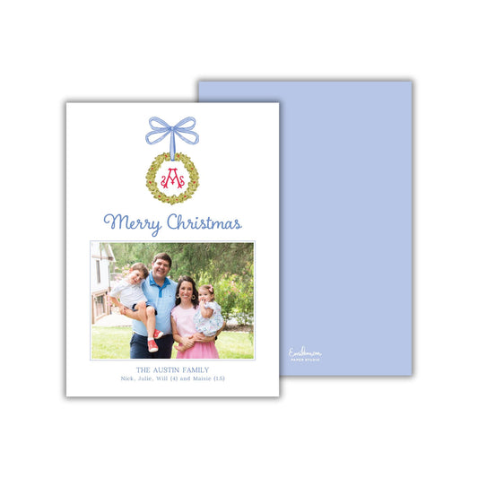The image is a Christmas card featuring a family photo of a man, woman, and child. The card has a blue background with a wreath and ribbon design, and the text &quot;Merry Christmas&quot; is displayed above the photo.