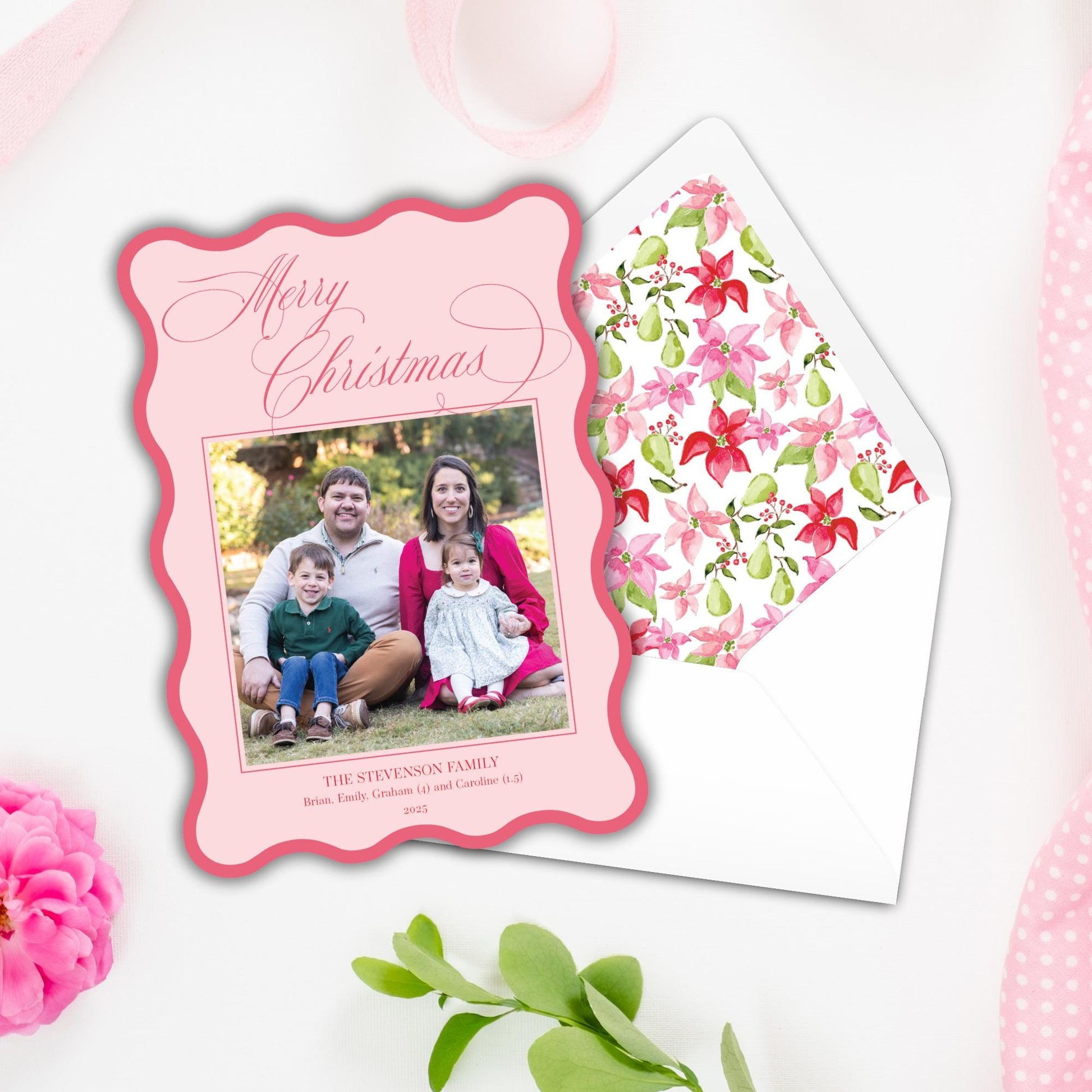 A pink Christmas card with a family photo of a man, woman, and two children, and a matching pink envelope with a floral pattern.
