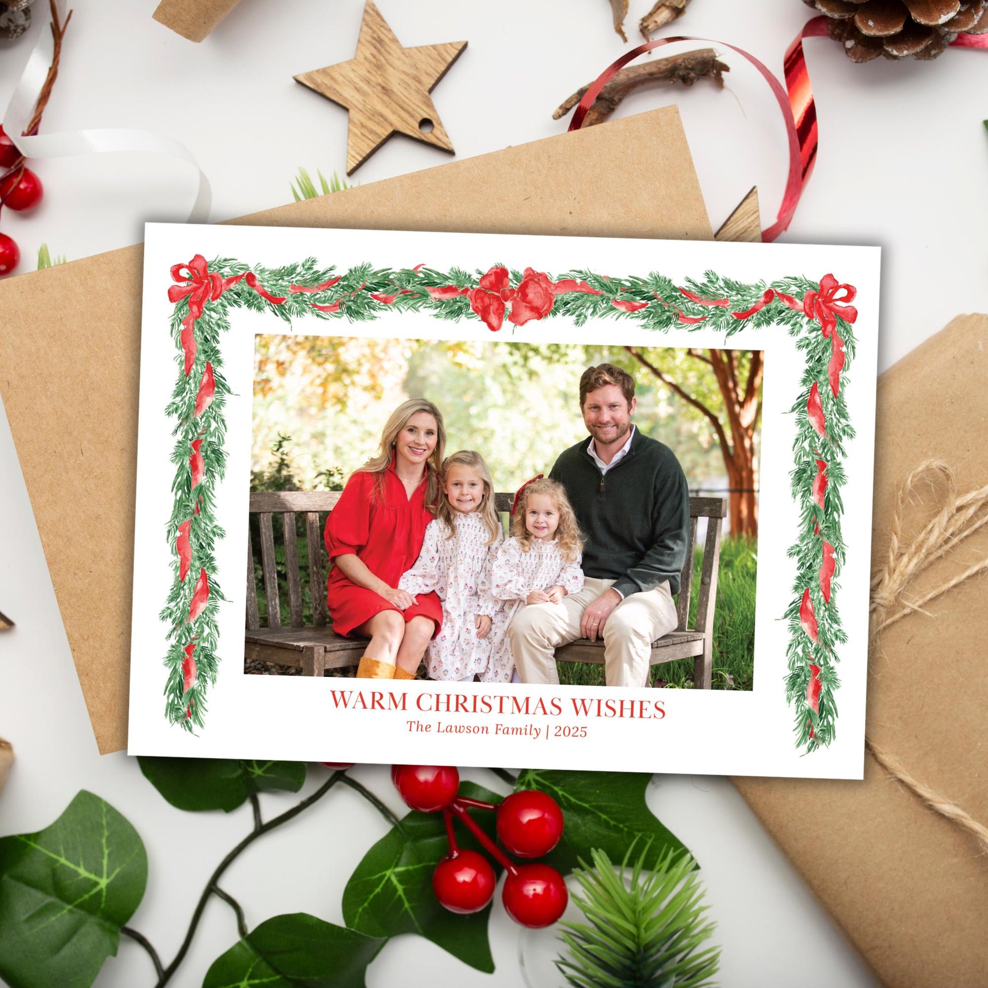 A family portrait of a man, woman, and two young girls, framed within a Christmas wreath and surrounded by holiday decorations such as pine cones, berries, and a star.