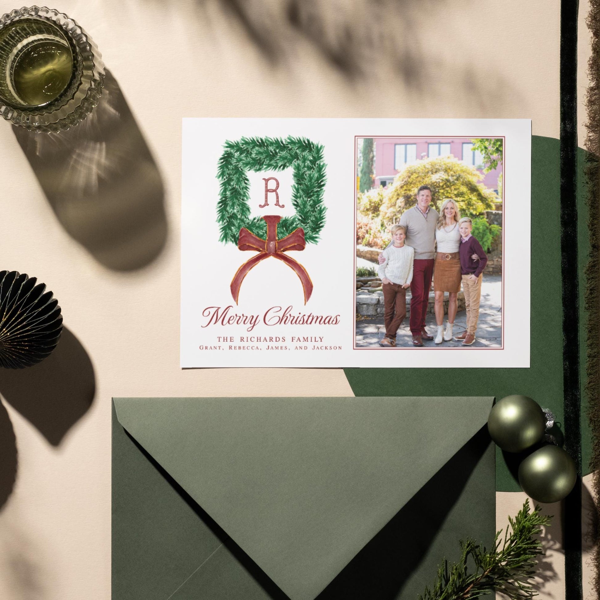 A Christmas card featuring a family photo and a wreath, along with a green envelope and some ornaments.