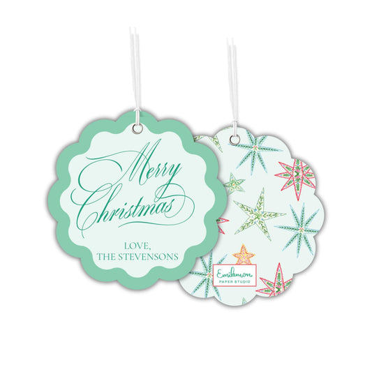 two Christmas-themed tags hanging from strings. The tag on the left has a scalloped edge and the text &quot;Merry Christmas&quot; written in cursive. The tag on the right has a star-shaped design with a floral pattern.